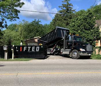 A dump truck and a waste bin parked in a driveway.
